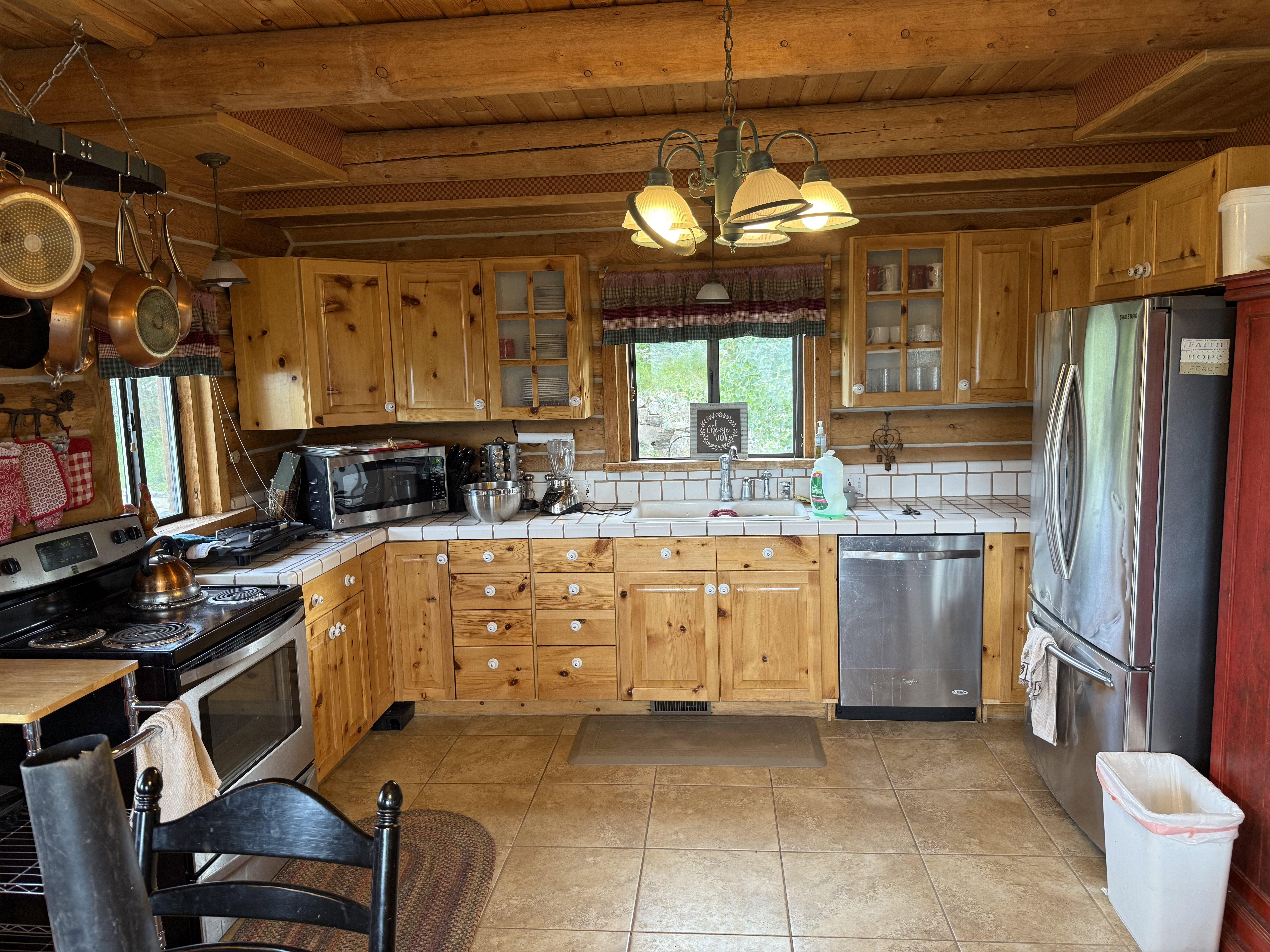 Kitchen featuring appliances with stainless steel finishes, tile countertops, a wooden ceiling with exposed beams, a chandelier, and decorative backsplash