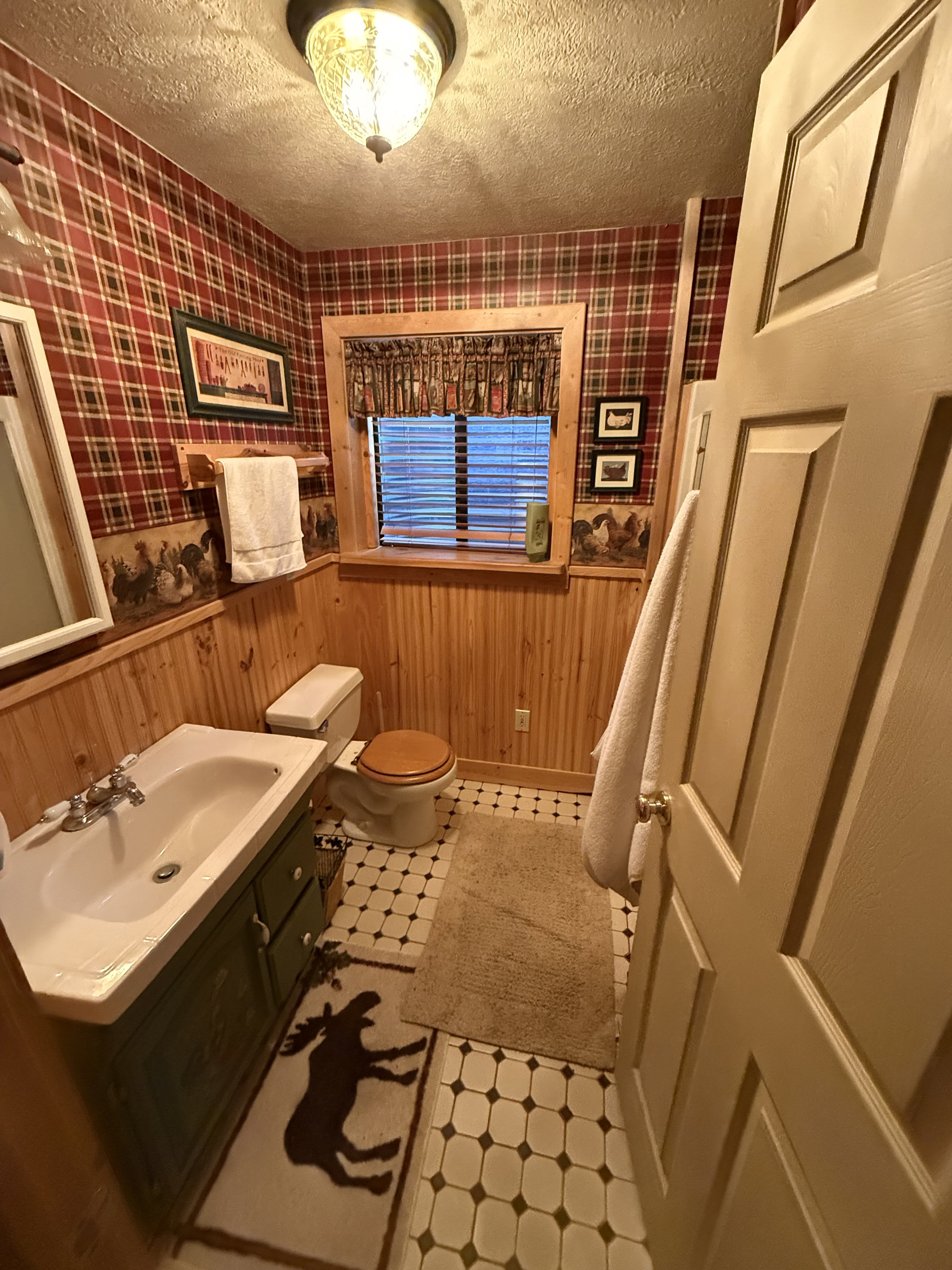 Half bathroom featuring tile patterned floors, wainscoting, wallpapered walls, a textured ceiling, and vanity