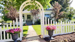 View of front of home featuring covered porch and rose arbor entrance.