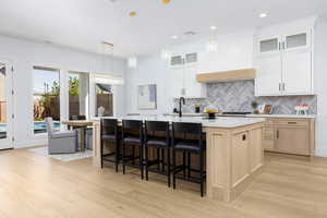 Dual tone kitchen with two tone color scheme, light stone counters, decorative light fixtures, a kitchen bar, and light wood-style flooring