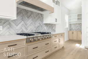 Kitchen featuring decorative backsplash, premium range hood, light wood finished floors, stainless steel gas cooktop, and light brown cabinets