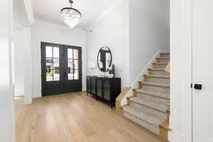 Entrance foyer with light wood finished floors, crown molding, hanging lights, and french doors