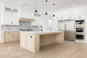 Kitchen featuring built in appliances, tasteful backsplash, light brown cabinetry, glass insert cabinets, and light wood finished floors