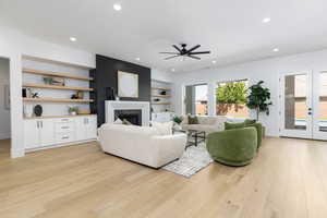 Living room featuring light wood-type flooring, a ceiling fan, recessed lighting, a premium fireplace, and built in shelves