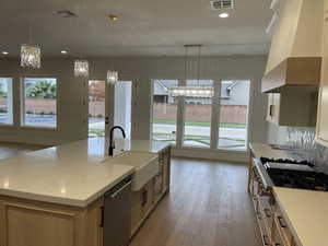 Kitchen with a chandelier, light wood-type flooring, pendant lighting, recessed lighting, and custom range hood