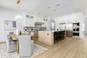 Two tone kitchen with stainless steel appliances, an island with sink, a kitchen bar, light wood-type flooring, and two tone color scheme