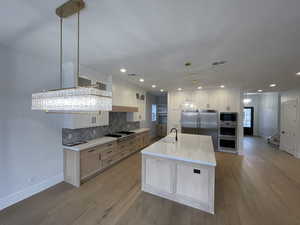 Kitchen featuring glass insert cabinets, tasteful backsplash, an island with sink, light stone counters, and built in appliances