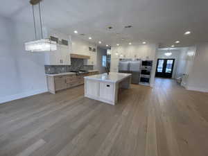 Kitchen with white cabinets, glass insert cabinets, tasteful backsplash, decorative light fixtures, and appliances with stainless steel finishes