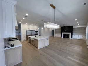 Kitchen featuring a kitchen island with sink, a fireplace, open floor plan, white cabinetry, and light stone countertops