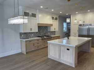 Kitchen featuring appliances with stainless steel finishes, hanging light fixtures, white cabinets, glass insert cabinets, and light brown cabinetry