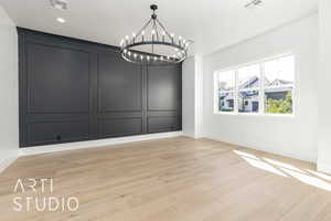 Unfurnished dining area with a chandelier, light wood-type flooring, and a decorative wall