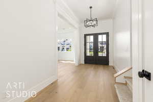 Foyer entrance featuring french doors, light wood finished floors, crown molding, a chandelier, and stairs