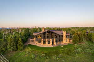 Back of house at dusk featuring a chimney, stone siding, a patio area, and a lawn