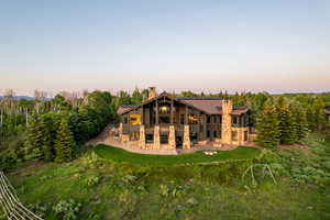 Back of property at dusk with stone siding, a chimney, a patio, and a lawn