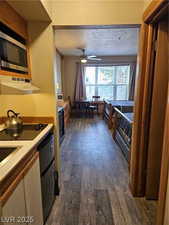 Kitchen with exhaust hood, stainless steel microwave, dark wood-type flooring, ceiling fan, and light countertops
