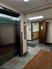 Hall with stone tile flooring, elevator, and a drop ceiling