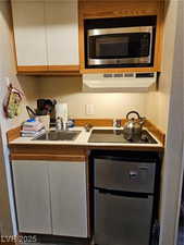 Kitchen featuring stainless steel microwave, under cabinet range hood, black electric stovetop, and white cabinetry