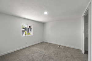 Carpeted empty room with a textured ceiling and recessed lighting