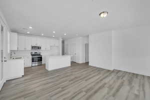 Kitchen with appliances with stainless steel finishes, recessed lighting, light countertops, light wood-style flooring, and a center island