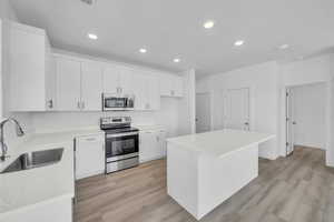 Kitchen featuring appliances with stainless steel finishes, light wood-type flooring, light countertops, white cabinetry, and recessed lighting