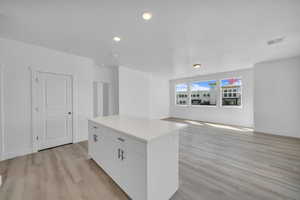 Kitchen featuring a kitchen island, light wood-type flooring, white cabinets, recessed lighting, and light countertops