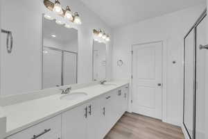 Bathroom featuring a shower stall, double vanity, and wood finished floors