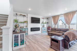Living room with wood finished floors, a glass covered fireplace, stairway, and recessed lighting