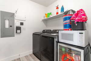 Laundry room with electric panel, washing machine and clothes dryer, light wood finished floors, and wine cooler