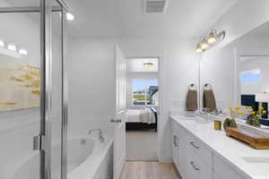 Ensuite bathroom with double vanity, plenty of natural light, a garden tub, and wood finished floors