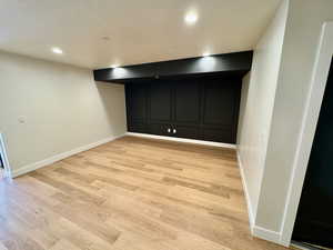Finished basement with a decorative wall, light wood-style floors, a textured ceiling, and recessed lighting