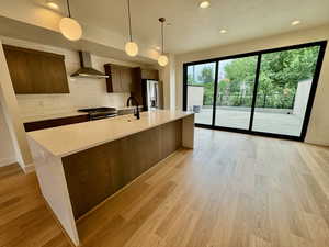 Kitchen featuring wall chimney range hood, appliances with stainless steel finishes, light countertops, modern cabinets, and a textured ceiling