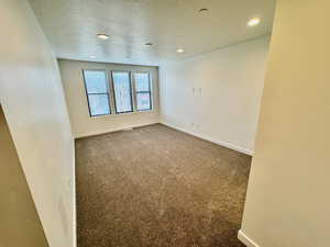 Unfurnished room featuring a textured ceiling, recessed lighting, and dark colored carpet