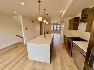 Kitchen with stainless steel gas range, wall chimney range hood, modern cabinets, light wood-style flooring, and recessed lighting