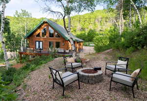 Rear view of property with an outdoor fire pit, a wooden deck, a view of trees, and log siding
