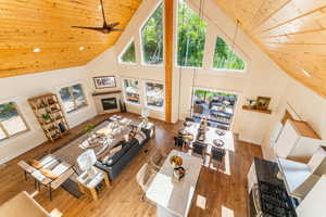 Living area featuring high vaulted ceiling, a glass covered fireplace, wooden ceiling, healthy amount of natural light, and wood finished floors