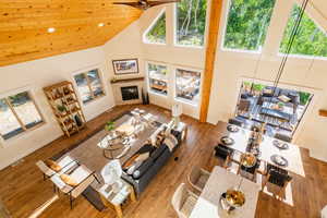Living room with high vaulted ceiling, healthy amount of natural light, a glass covered fireplace, wood finished floors, and ceiling fan