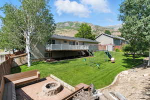 Rear view of house featuring a playground, a fire pit, a deck with mountain view, a fenced backyard, and a garden