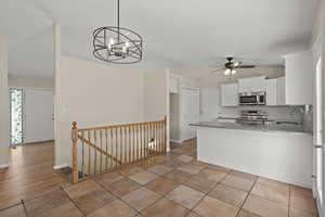 Kitchen with stainless steel appliances, vaulted ceiling, light granite countertops, white cabinetry, and tile backsplash