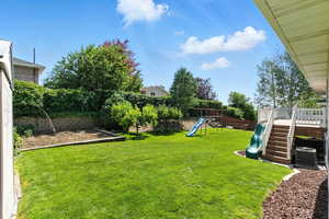 Fenced backyard with a playground, garden, fruit trees (peach and apple) and deck