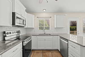 Kitchen featuring stainless steel appliances, light tile patterned floors, a peninsula, white cabinetry, and tile backsplash