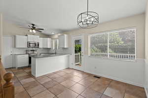 Kitchen with stainless steel appliances, a peninsula, white cabinetry, tile backsplash, and light tile patterned flooring