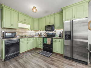 Kitchen featuring black appliances, wood finished floors, tasteful backsplash, and stone countertops