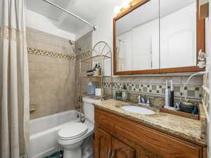 Full bath with shower / bath combo with shower curtain, vanity, and decorative backsplash