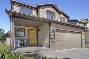 Townhome / multi-family property with stone siding, a porch, concrete driveway, and an attached garage