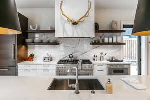 Kitchen with open shelves, high quality appliances, decorative backsplash, light countertops, and white cabinetry