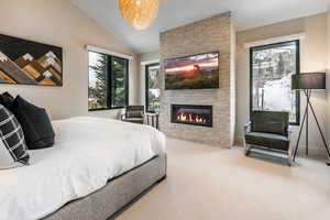 Bedroom with vaulted ceiling, carpet, and a stone fireplace