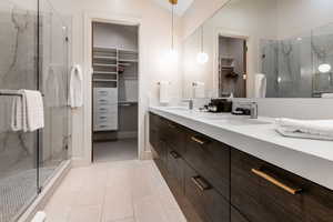 Bathroom with a spacious closet, a marble finish shower, double vanity, tile patterned flooring, and lofted ceiling