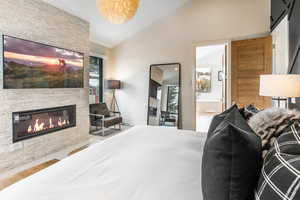 Bedroom with a stone fireplace, tile patterned floors, and high vaulted ceiling
