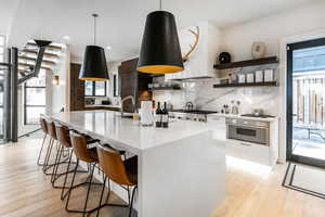 Kitchen with appliances with stainless steel finishes, light wood-type flooring, light countertops, decorative backsplash, and a kitchen breakfast bar