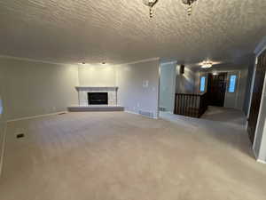 Unfurnished living room featuring a textured ceiling, carpet flooring, a fireplace with raised hearth, and crown molding